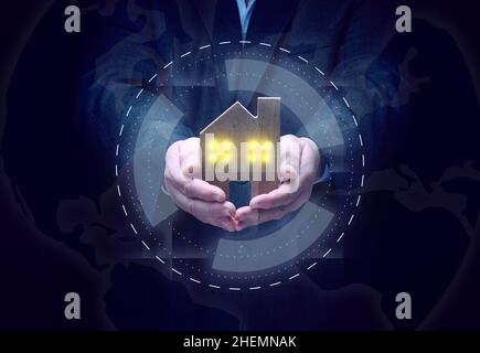 Geschäftsmann in einem Anzug hält ein Holzmodell eines Hauses auf dunklem Hintergrund. Immobilienverkauf und Kauf Konzept, Miete. Versicherungen und Hypotheken Stockfoto
