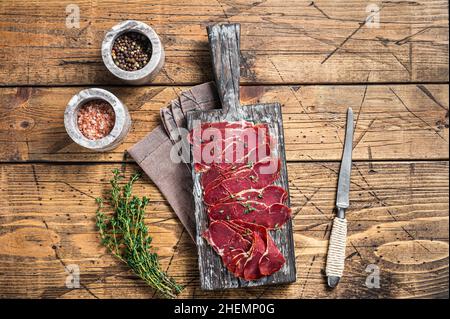 Getrocknete Pastrami-Scheiben, Rinderfleisch mit Kräutern auf Holzbrett. Holzhintergrund. Draufsicht Stockfoto