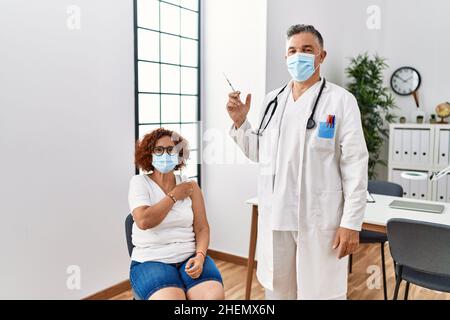 Frau mittleren Alters, die vom Arzt geimpft wird, sieht positiv aus und ist glücklich, steht und lächelt mit einem selbstbewussten Lächeln, das Zähne zeigt Stockfoto