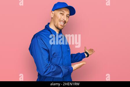 Glatze Mann mit Bart tragen Baumeister Jumpsuit Uniform einladend lächelnd natürlich mit offener Hand betreten Stockfoto