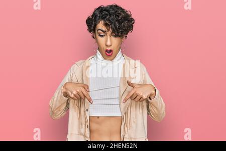 Schöner Mann mit Make-up und Frauenkleidung zeigt nach unten, mit Fingern, die Werbung zeigen, überraschendes Gesicht und offenen Mund Stockfoto