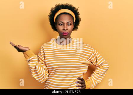 Junge afroamerikanische Frau präsentiert mit offenen Handflächen, hält etwas skeptisch und nervös, runzelte die Stirn wegen des Problems. Negative Person. Stockfoto