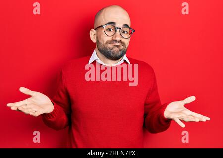 Junger kahlköpfiger Mann in lässiger Kleidung und Brille, ahnungsloser und verwirrter Ausdruck mit erhobenen Armen und Händen. Zweifelskonzept. Stockfoto