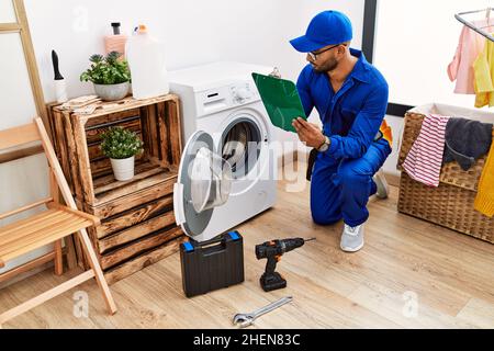 Junger arabischer Mann mit Techniker-Uniform, der in der Waschküche auf der Zwischenablage schrieb Stockfoto