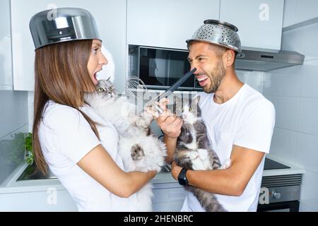 Mann und Frau kämpfen in der Küche mit ihren schönen Katzen. Junges Paar mit Spaß zu Hause. Paar spielt mit lustigen Haustieren. Stockfoto