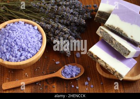 Meersalz mit Lavendel in einer Bambusschale befinden sich Seife aus Lavendel, Olivenöl und Kakaobutter auf einem Bambusteller und getrocknete Lavendelblüten Stockfoto
