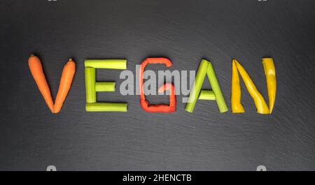 Veganes Essen und veganes Diät-Konzept. Wort vegan mit Gemüse auf schwarzem Hintergrund geschrieben Stockfoto