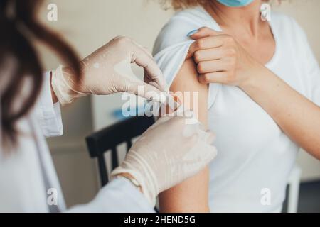 Nahaufnahme Porträt eines Arztes Hände, die nach Injektion eines Corona-Virus-Impfstoffes einen Gips auf den weiblichen Arm legen. Medizinische Behandlung. Stockfoto
