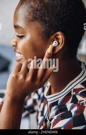 Seitenansicht Porträt einer lächelnden afrikanischen Frau, die Musik in airpods hört. Nahaufnahme Porträt. Stockfoto