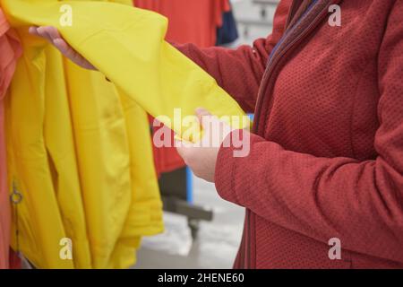 Kaukasische Frau wählt gelben Windbreaker aus dem Regen im Laden zu kaufen Stockfoto