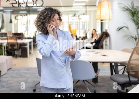 Fokussierte Geschäftsfrau in formeller Kleidung im Büro stehend und am Telefon sprechend. Stockfoto
