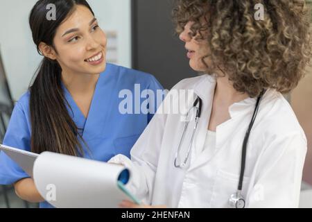 Junge Krankenschwester in blauer Uniform lächelt und spricht mit einem Arzt. Stockfoto