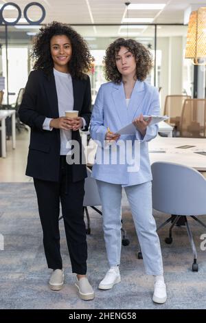 Zwei hübsche Geschäftsfrauen tragen formelle Kleidung und lächeln und schauen im Büro auf die Kamera. Stockfoto