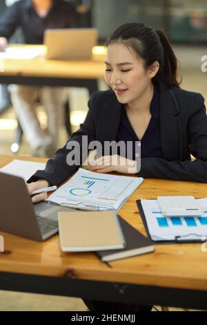 Elegante asiatische junge Geschäftsfrau, die einen Geschäftsfinanzbericht auf ihrem Laptop-Computer erstellt. Stockfoto