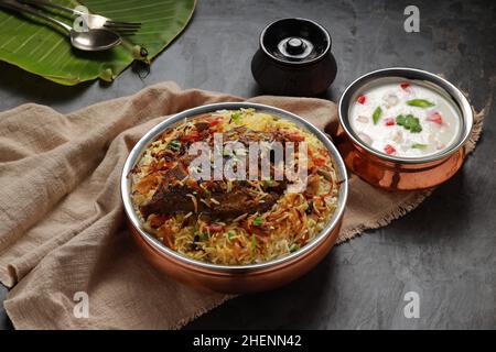 Fisch Biriyani, südindischer Art Fisch biriyani traditionell in einem Messinggefäß mit Raitha als Beilage angeordnet. Stockfoto