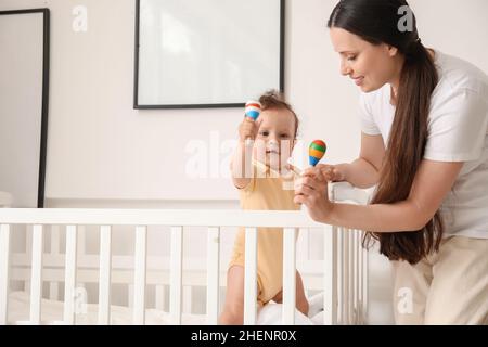 Junge Mutter gibt ihrem kleinen Baby Spielzeug in der Krippe zu Hause Stockfoto