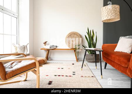 Moderne Bank mit Pouf, Kissen und Holzhand im Inneren des hellen Wohnzimmers Stockfoto