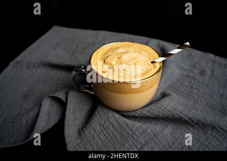 Goldener Dalgona-Kaffee auf einem Tisch mit grauer Tischdecke und schwarzem Hintergrund Stockfoto