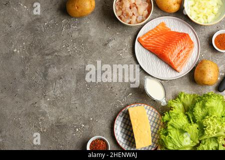 Teller mit frischem Lachs und Zutaten für die Zubereitung des englischen Fischpastete auf grauem Hintergrund Stockfoto