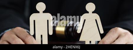 Holzfiguren von Mann und Frau in den Händen des Richters vor dem Hintergrund des Richters Hammer Stockfoto