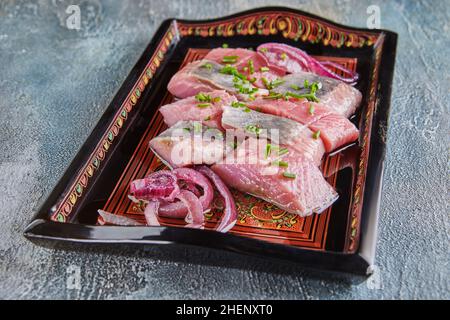 Roter Hering mit Zwiebeln und Kräutern auf Tablett Stockfoto