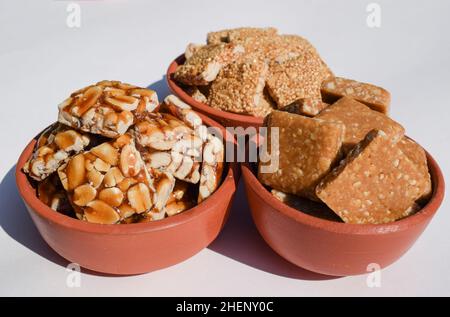 Peanut Chikki, zerkleinerte roaste Peanut Chiki, Rajgiri Chikki oder Amaranth-Sprödriegel. Jaggery mit Erdnussbonbons serviert in irdenen Schüsseln Topf während Stockfoto