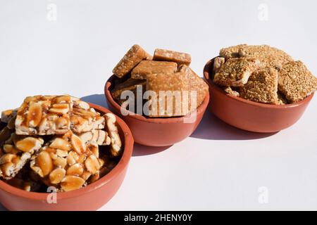 Peanut Chikki, zerkleinerte roaste Peanut Chiki, Rajgiri Chikki oder Amaranth-Sprödriegel. Jaggery mit Erdnussbonbons serviert in irdenen Schüsseln Topf während Stockfoto