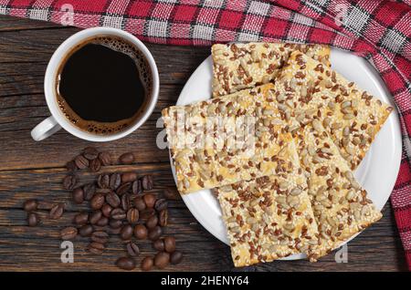 Tasse Kaffee und Kekse mit Sonnenblumenkernen und Sesam in Teller befindet sich auf dem alten Holztisch, Draufsicht Stockfoto