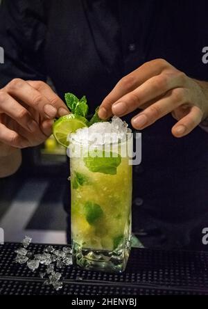 Ein Barkeeper verleiht einem leckeren frisch zubereiteten Mojito-Cocktail den letzten Schliff, indem er Dekorationen hinzufügt Stockfoto
