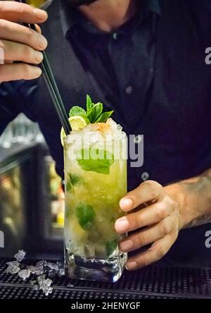 Ein Barkeeper fügt einem frisch zubereiteten Mojito-Cocktail an einer Bar Trinkhalme hinzu Stockfoto