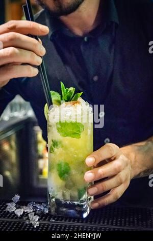 Ein Barkeeper fügt einem frisch zubereiteten Mojito-Cocktail in einem Nachtclub Trinkhalme hinzu Stockfoto