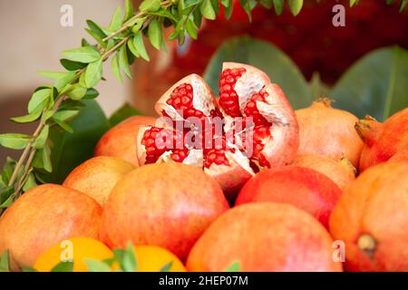 Zerbrochener Granatapfel und ganze Früchte, zubereitet für frisch gepressten Saft im Korb, der mit frischen grünen Blättern verziert ist Stockfoto