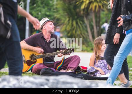 Straßenmusiker spielt Gitarre und das kleine Mädchen hört ihm auf dem Rasen im Park von Moda, Kadikoy Bezirk in Istanbul, Türkei. Stockfoto