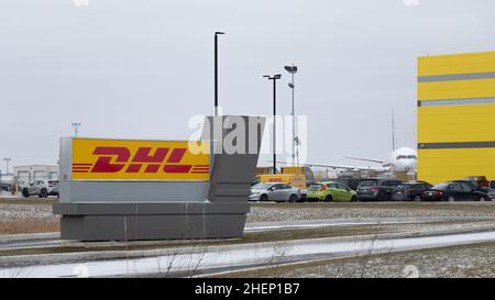 Vor einer neuen Frachtanlage am Flughafen Hamilton befindet sich ein DHL-Schild, im Hintergrund ist ein Frachtflugzeug zu sehen. Stockfoto