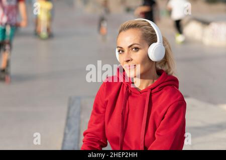 Eine sportliche Frau, die Kopfhörer verwendet und die Kamera anschaut und im Freien sitzt Stockfoto