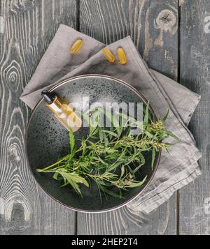 Glasflasche mit CBD-Öl, THC-Tinktur und Hanfblatt eine schwarze Platte auf einem hölzernen Hintergrund. Natürlichkeit. CBD-Öl-Kosmetik. Stockfoto