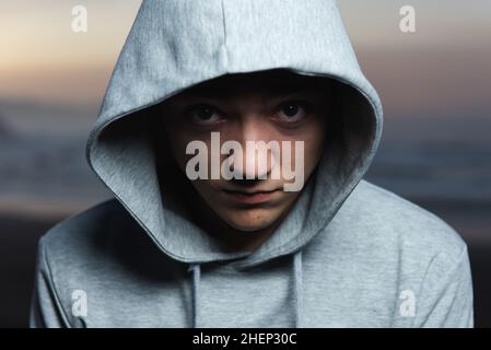 Dramatisches Porträt eines ernsthaften hispanischen Teenagers, der auf die Kamera schaut und einen Hoodie trägt. Stockfoto