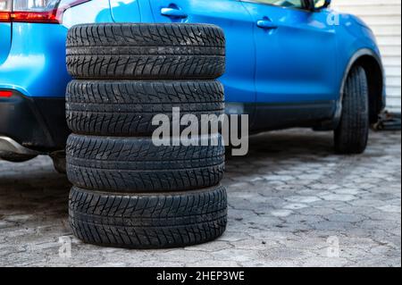 Satz von Winterreifen neben dem Auto im Radservice, das Konzept des saisonalen Reifenwechsels Stockfoto