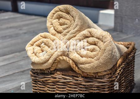 Drei gerollte beigefarbene Handtücher in einem strohgedeckten Rattankorb. Stockfoto