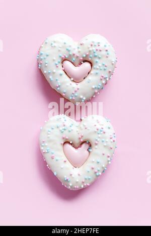 Flache Lage von zwei herzförmigen Lebkuchenkekse mit Streuseln und Glasur auf rosa Hintergrund. Blick von oben auf die leckere Bäckerei am Valentinstag, hausgemachter Bäcker Stockfoto