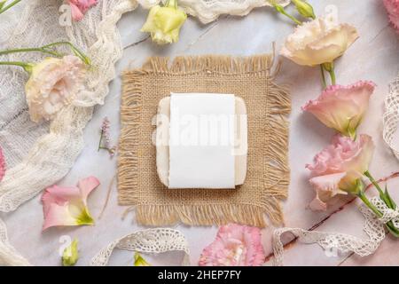 Seifenstück auf einem Marmortisch mit rosa Blumen, Blütenblättern und Vintage-Bändern, Draufsicht. Seifenmockup Stockfoto
