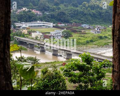 Eine Weitwinkelaufnahme einer Betonbrücke, die über einem Fluss mit Bäumen und Gebäuden in Indien errichtet wurde. Stockfoto