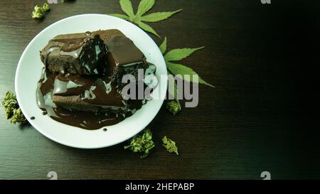 Bio Bio hausgemachte und gebackene Hush Brownies aus Amsterdam, bedeckt mit dunklem 85% Chcolate. Topfblätter und Unkrautknospen auf Holztisch. THC cbd gesund Stockfoto