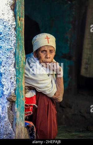 Alte äthiopische Frau mit rotem Kreuz auf der Mütze, die von der Tür schaut Stockfoto