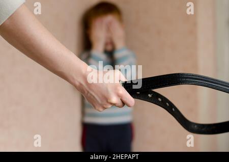 Mama mit Gürtel steht vor dem Kind. Der Sohn weint in der Ecke. Häusliche Gewalt gegen Kinder. Stockfoto