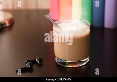 Glasbecher mit heißem Latte auf purpurpurem Schreibtisch, Kopfhörer und Bücher mit lgbt-Bewegungsfarben Stockfoto