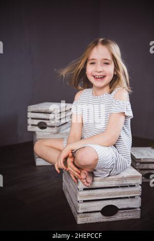 Porträt eines glücklichen Teenager-Mädchen im Sommerkleid im Studio. Sie sitzt auf den Boxen, der Wind weht ihr die Haare. Schönheit und Mode. Speicherplatz kopieren Stockfoto