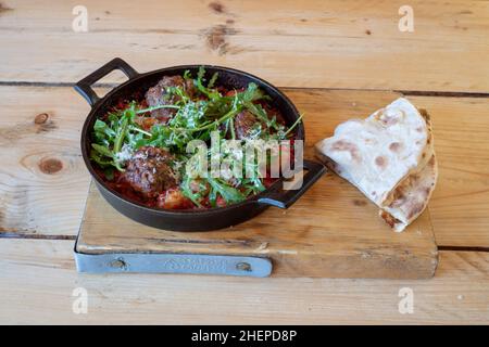 Italienische Sizzler Fleischbällchen & Gnocchi in Tomatensauce Bolognaise in einer heißen gusseisernen Pfanne serviert Stockfoto