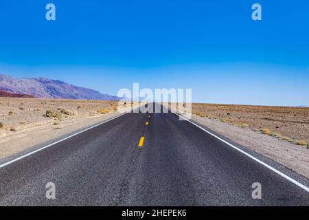 Leere Straße durch die Wüste des Death Valley unter blauem Himmel Stockfoto