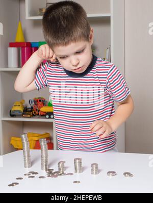 Ein junger Geschäftsmann im Vorschulalter denkt über Finanzen nach und plant, Geld und Münzen auszugeben. Stockfoto